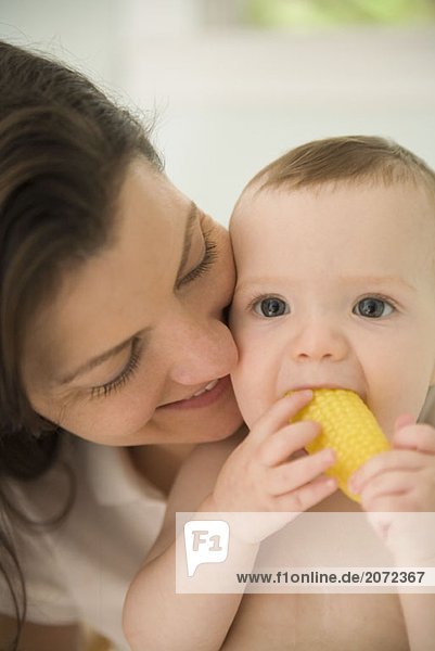 Eine Mutter betrachtet ein Baby mit Plastikgemüse im Mund