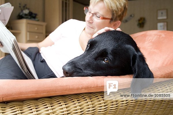 Woman reading newspaper with dog on couch
