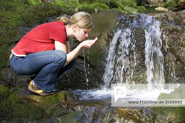Young woman drinking water from stream  side view