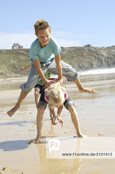 Boy and girl playing leapfrog on beach