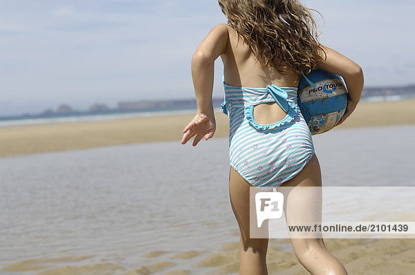 Rear view of girl running with ball on beach