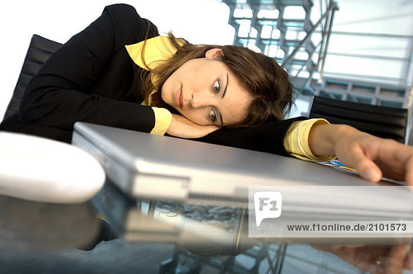 Young businesswoman leaning on glass table by laptop
