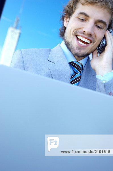 Young businessman using mobile phone and laptop  smiling