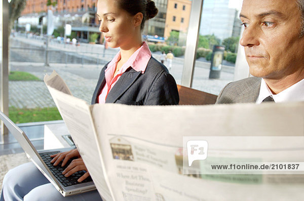 Businesswoman working on laptop while businessman reading newspaper
