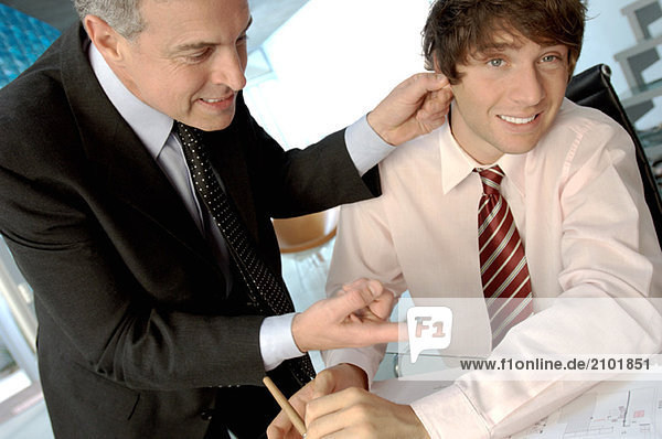 Businessman holding ear of colleague in office