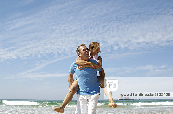 Man piggybacking woman on beach