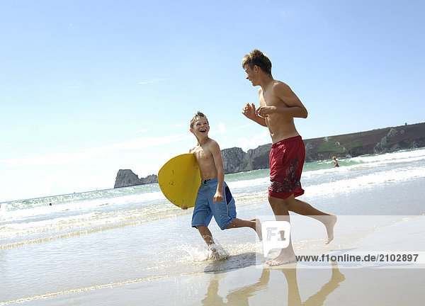Side profile of two brothers running on beach