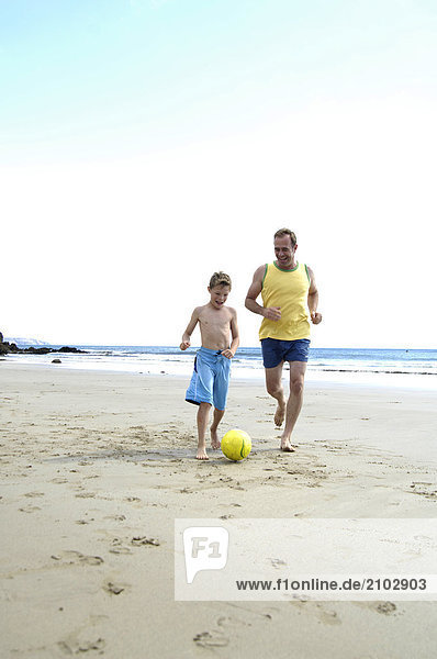 Father playing soccer with his son on beach