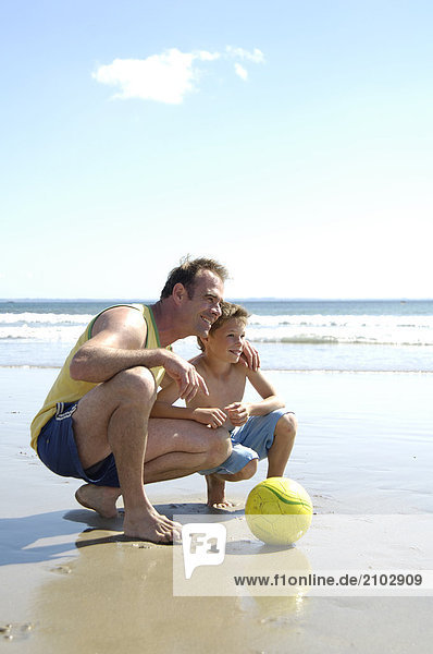 Vater hockend mit seinem Sohn am Strand