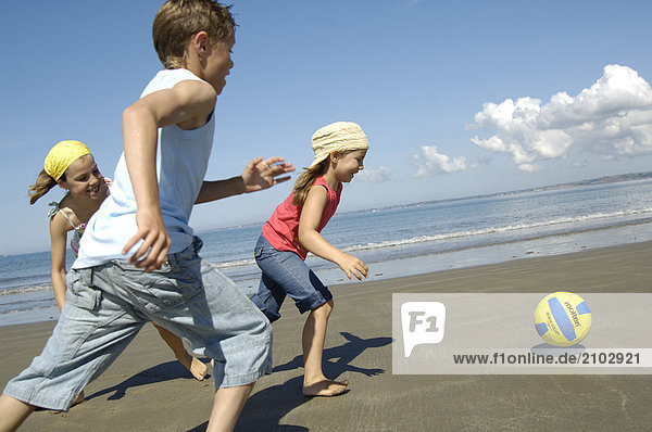 Drei Kinder spielen Fußball am Strand