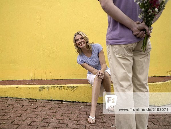 Woman looking at man hiding bouquet of flowers