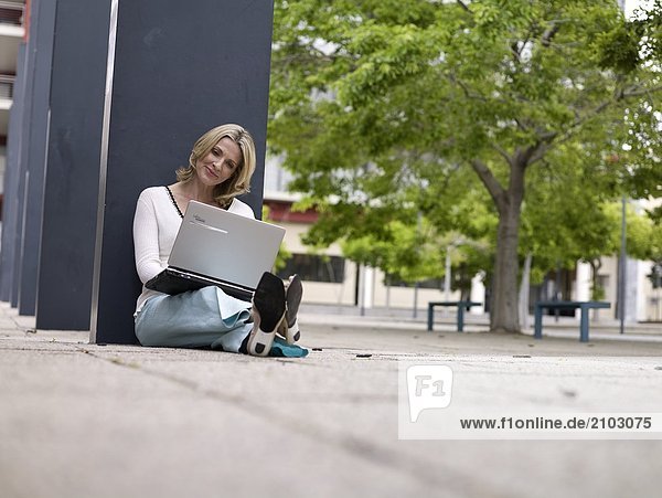 Geschäftsfrau am Straßenrand sitzen und mit laptop