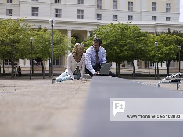 Geschäftsfrau und Businessman sitting in der Nähe von Brunnen mit laptop