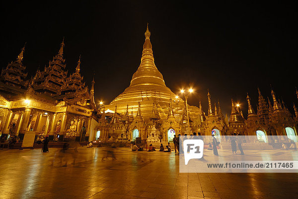 Group of people at Buddhist temple lit up during dusk  Shwedagon Pagoda  Yangon  Myanmar