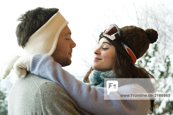Junges Paar in Winterkleidung  Frau mit Armen um den Hals  Seitenansicht