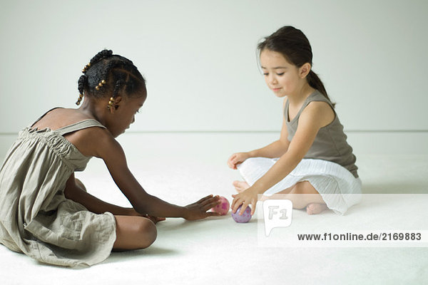 Zwei Mädchen sitzen auf dem Boden und spielen mit Spielzeugbällen.