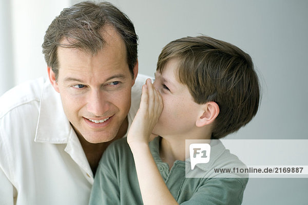 Boy whispering in father's ear  close-up