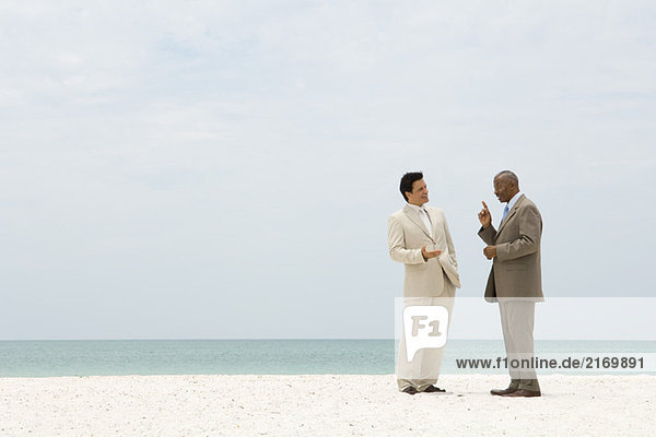 Zwei Geschäftsleute  die von Angesicht zu Angesicht am Strand stehen und sich unterhalten.