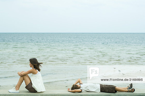 Zwei junge Freunde schauen auf den Ozean  einer sitzt  der andere liegt auf dem Rücken.