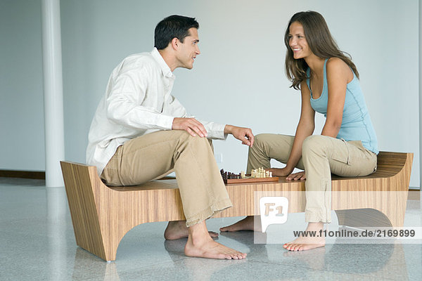 Junges Paar spielt Schach  lächelt sich an.