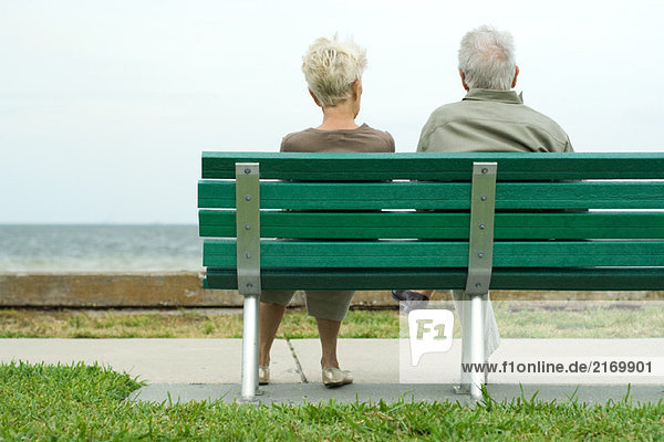 Paar auf Bank sitzend mit Blick auf den Ozean  Rückansicht