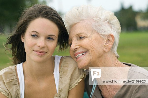 Seniorin  die den Kopf auf die Schulter der Teenager-Enkelin lehnt  lächelnd und wegschauend.