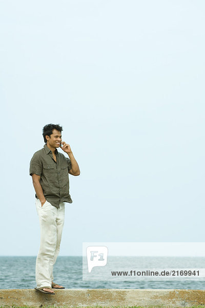 Mann steht mit Handy  Ozean im Hintergrund