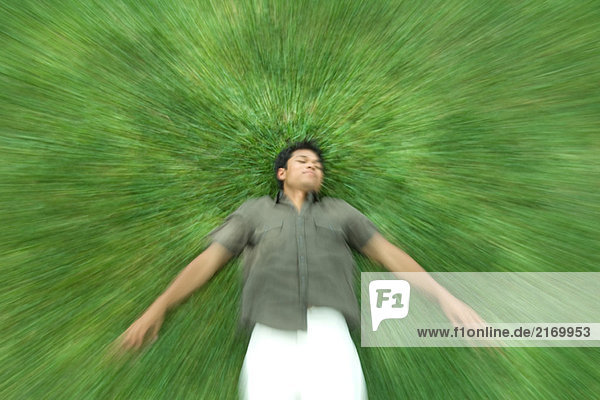 Mann auf dem Rücken im Gras liegend mit geschlossenen Augen  verschwommene Bewegung