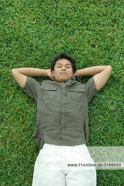 Mann auf dem Rücken im Gras liegend  mit Händen unter dem Kopf  Augen geschlossen.
