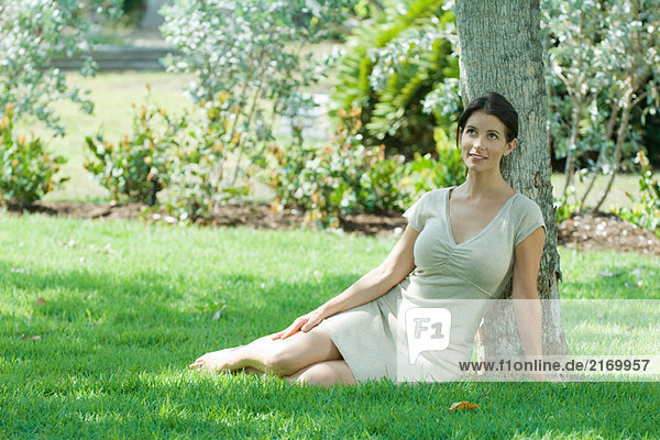 Woman sitting on the ground under tree  smiling  looking up