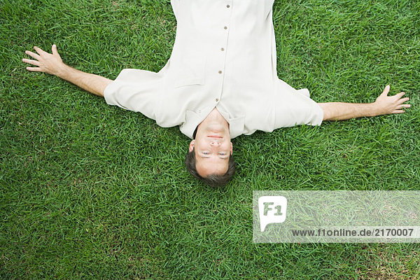 Man lying on back on grass  smiling at camera  viewed from directly above