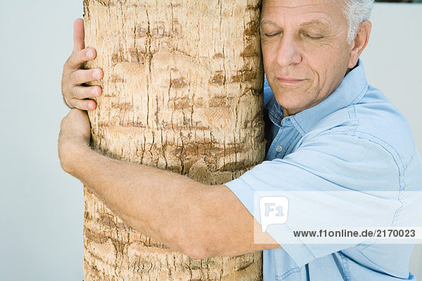 Mature man hugging tree trunk  eyes closed  smiling