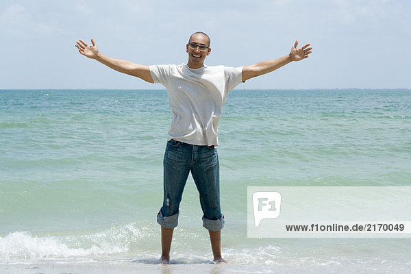 Man standing ankle deep in ocean with arms outstretched  smiling at camera