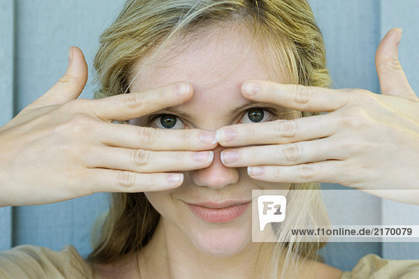 Woman peeking through fingers at camera