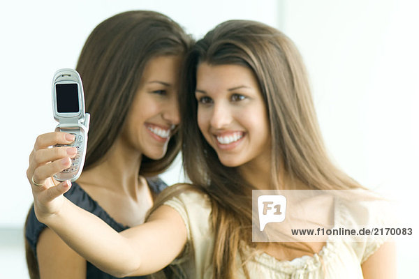 Twin teenage girl photographing self and sister with cell phone  both smiling