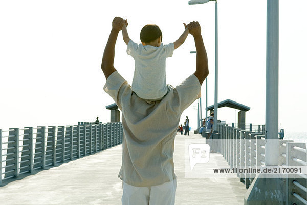 Father carrying son on shoulders  holding hands  rear view