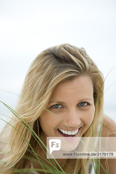Woman smiling at camera through tall grass  portrait
