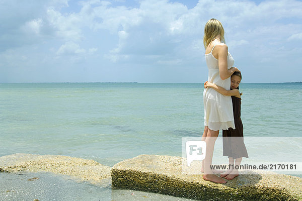 Mutter und Tochter stehen am Rande des Meeres  umarmend  volle Länge