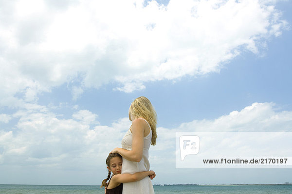 Mädchen umarmende Mutter  Ozeanhorizont und Himmel im Hintergrund