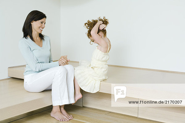 Mother and little girl  sitting together  smiling  girl holding up hair