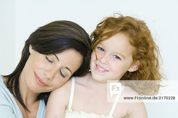 Mother and daughter  woman resting head on girl's shoulder  girl smiling at camera