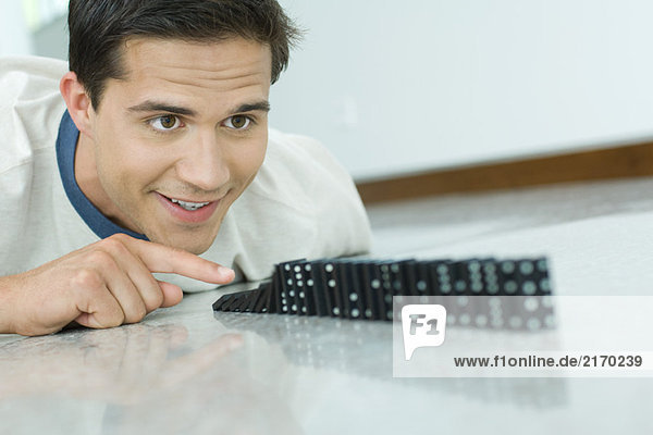 Young man knocking over line of dominos