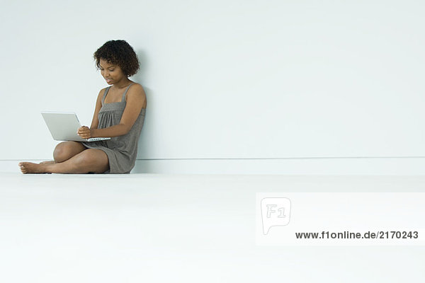 Junge Frau auf dem Boden sitzend  mit Laptop
