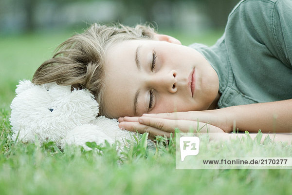 Junge ruht Kopf auf Teddybär  schläft auf Gras