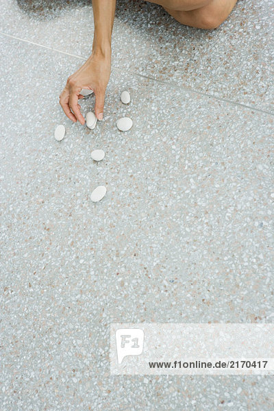 Frau arrangiert Kieselsteine auf dem Boden  abgeschnittene Handansicht