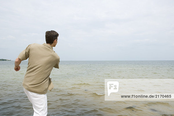 Mann beim Abschöpfen von Steinen am Strand  Rückansicht