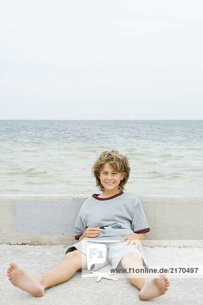 Junge sitzt mit Seestern auf dem Boden und lächelt in die Kamera.