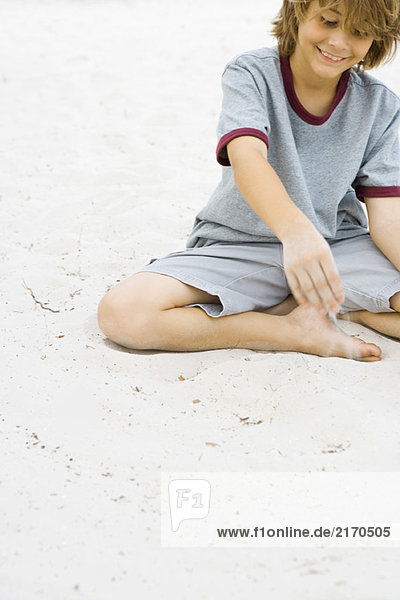 Junge spielt im Sand  lächelnd  mit abgeschnittenem Blick