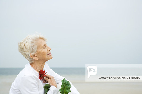 Seniorin mit Gerbera-Gänseblümchen an der Brust  Augen geschlossen  Profil