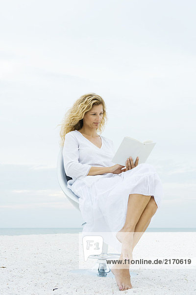 Woman sitting in chair at the beach  reading book